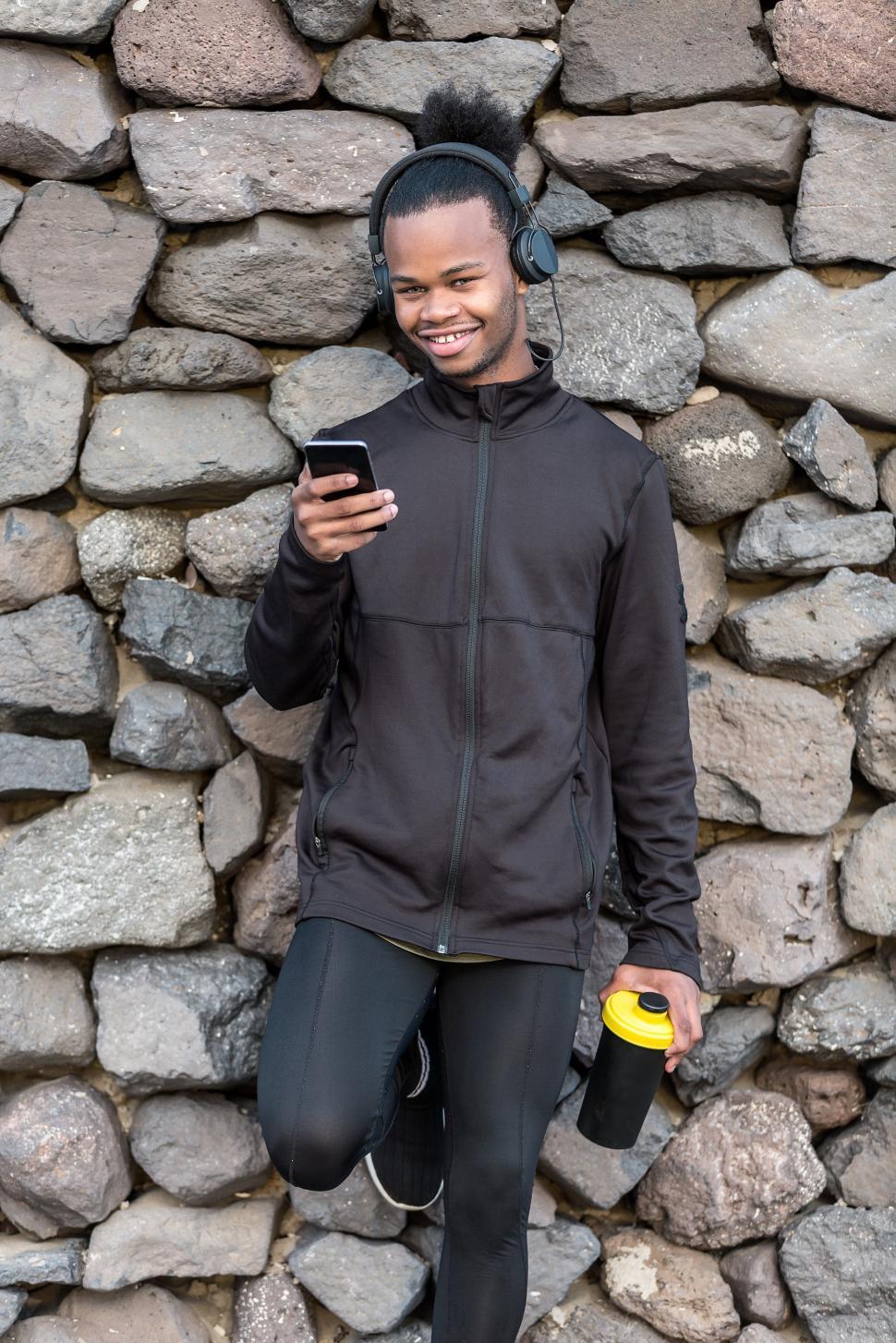 Free Image of Cheerful black guy with smartphone and cup near stone wall 