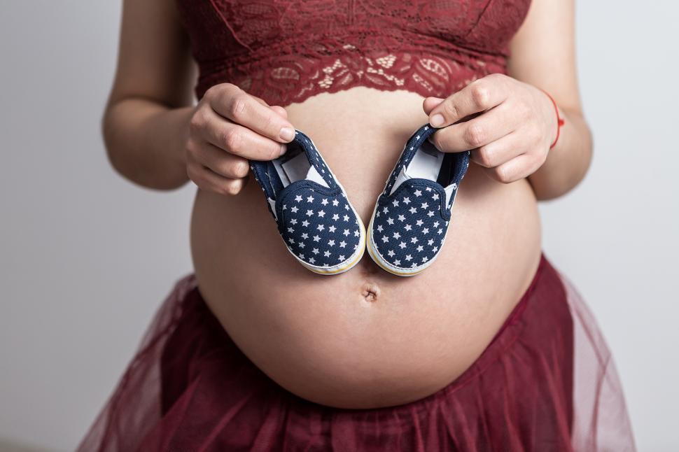 Free Image of Crop of female holding baby shoes on pregnant stomach 
