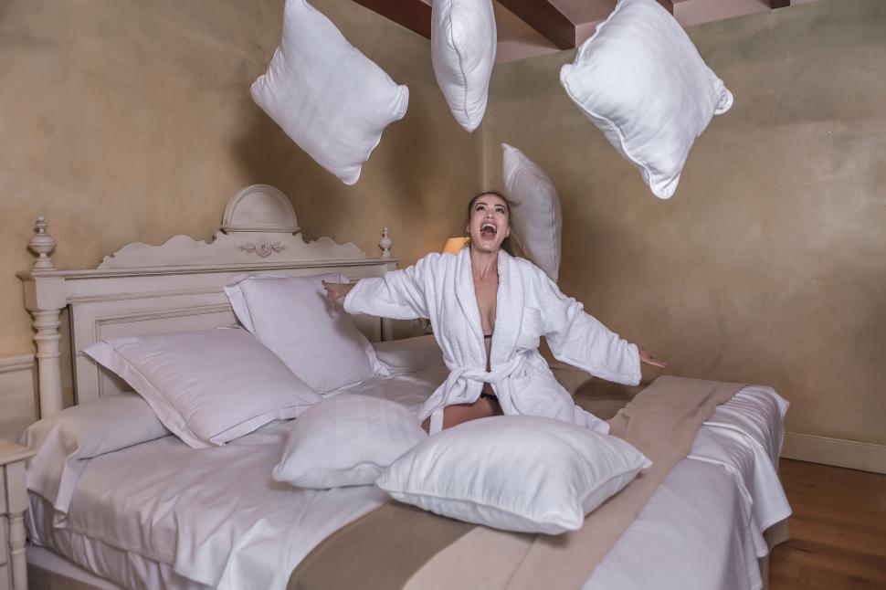 Free Image of Cheerful woman throwing up pillows on bed 