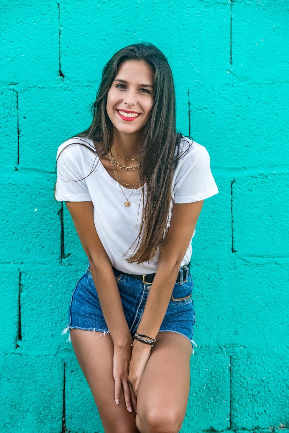 Free Image of Beautiful stylish female standing by wall and smiling 