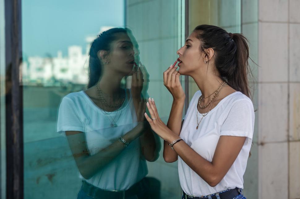 Free Image of Young woman applying makeup near glass wall 