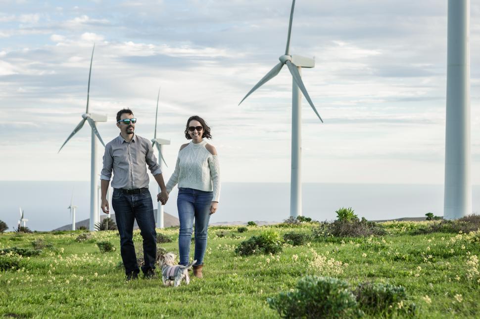 Free Image of Happy couple walking with dog in field with windmills 