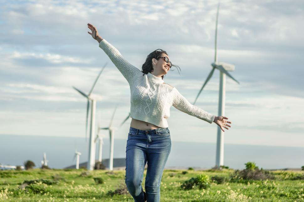 Free Image of Carefree woman standing in field with windmills on sunny day 