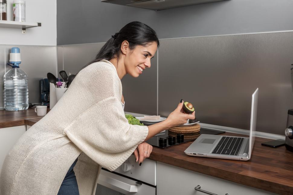 Free Image of Woman cooking in kitchen and having video call on laptop 