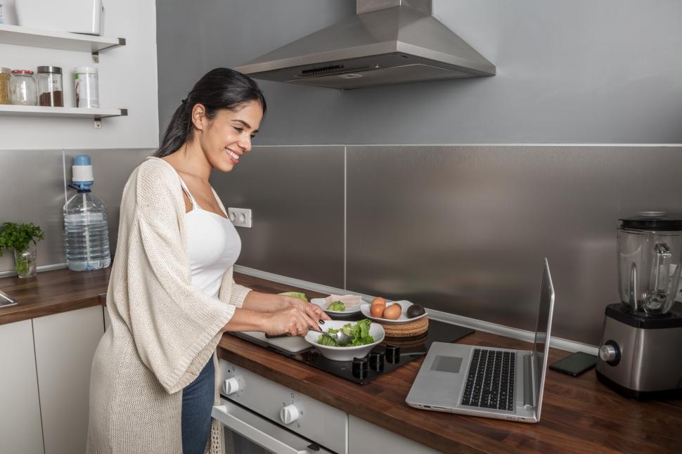 Download Free Stock Photo of Smiling woman cooking salad and watching video on netbook 