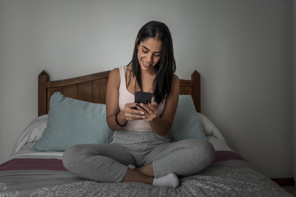 Free Image of Cheerful woman messaging on smartphone on bed 