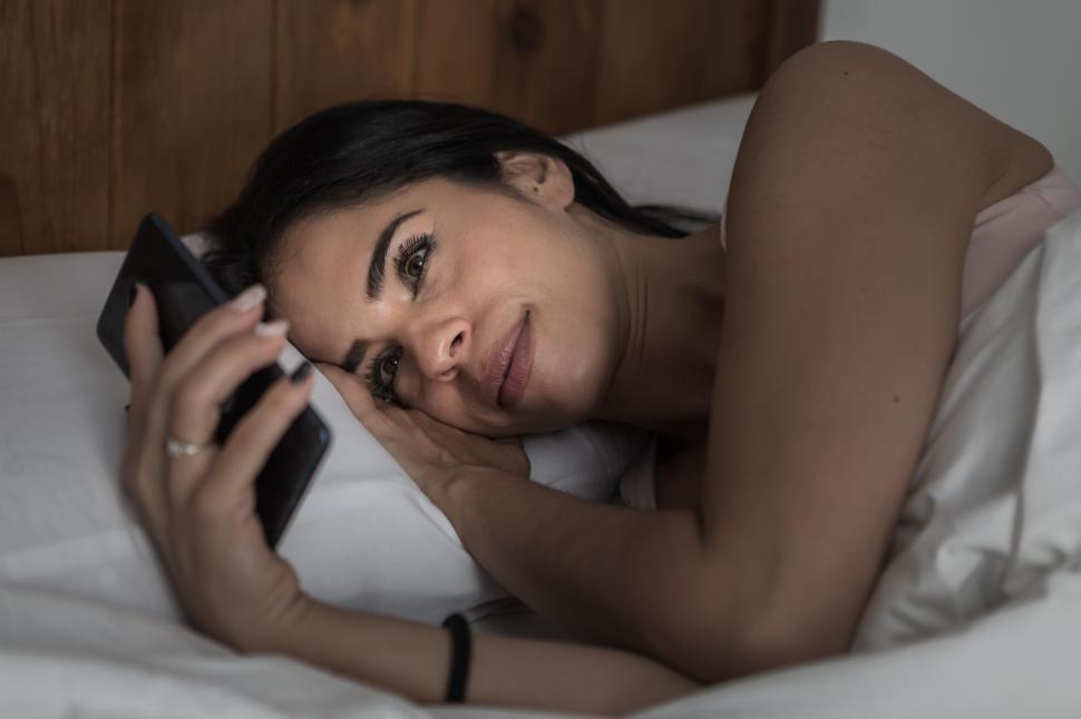 Free Image of Content woman lying in bed and browsing smartphone 