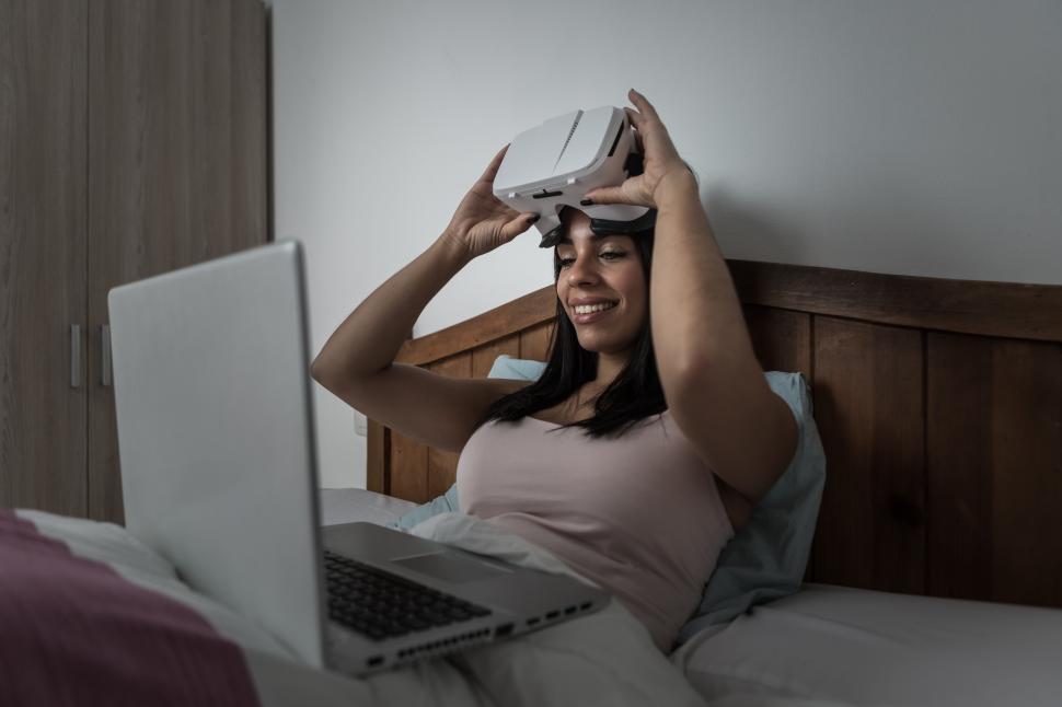 Free Image of Woman using VR goggles and laptop while in bed 