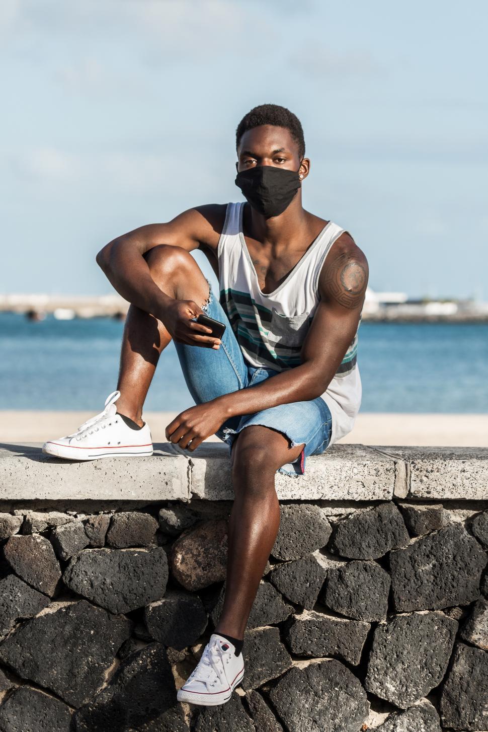 Free Image of Black man in mask and with smartphone on seashore 