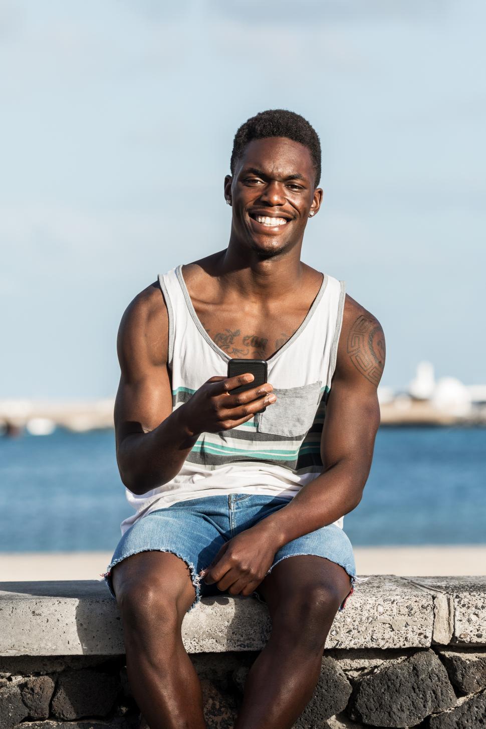 Free Image of Smiling man using smartphone on embankment 