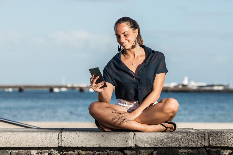 Free Image of Smiling woman using smartphone on embankment in summer 