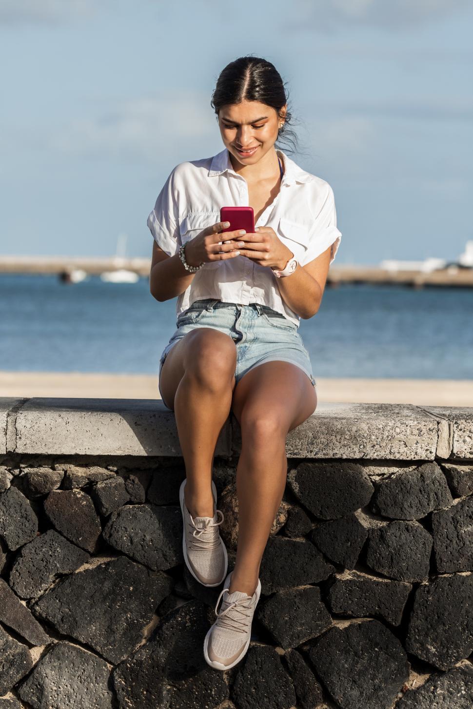 Free Image of Smiling woman messaging on mobile phone at seafront 