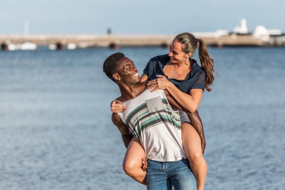 Free Image of Black man giving piggyback ride to woman near sea 