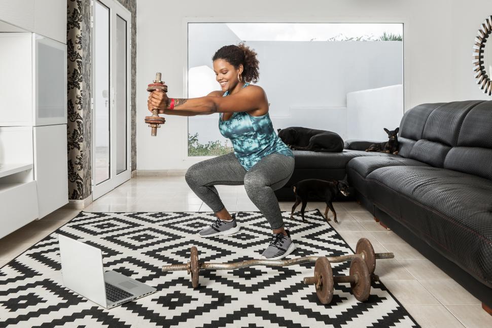 Free Image of Black sportswoman doing squats with dumbbell at home 