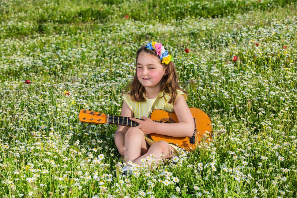 Free Image of Little girl with ukulele resting in field 