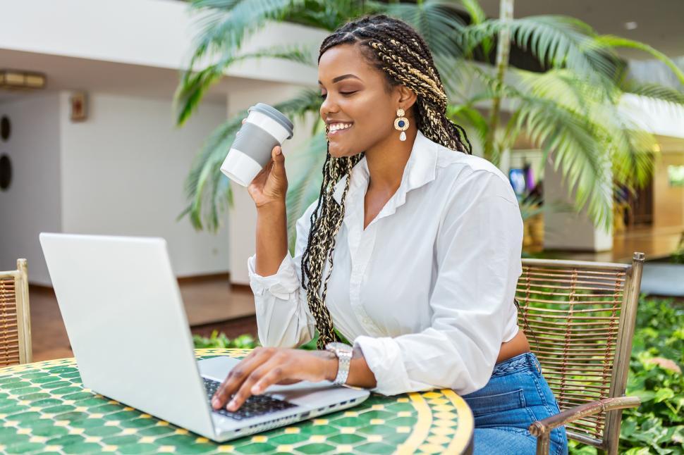 Free Image of Cheerful African American woman using laptop and holding cup of 
