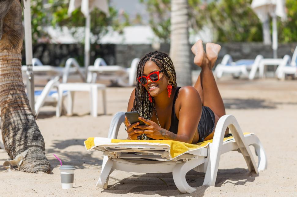 Download Free Stock Photo of African American woman on the beach lying on a deck chair using phone 