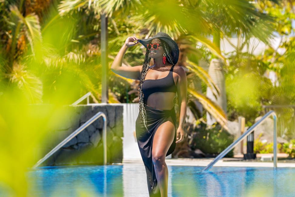 Download Free Stock Photo of View through leaves of an African American woman standing by the pool 
