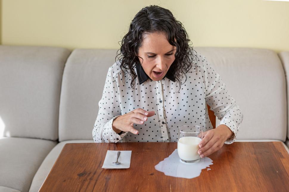 Free Image of Woman spills a glass of milk on the table 