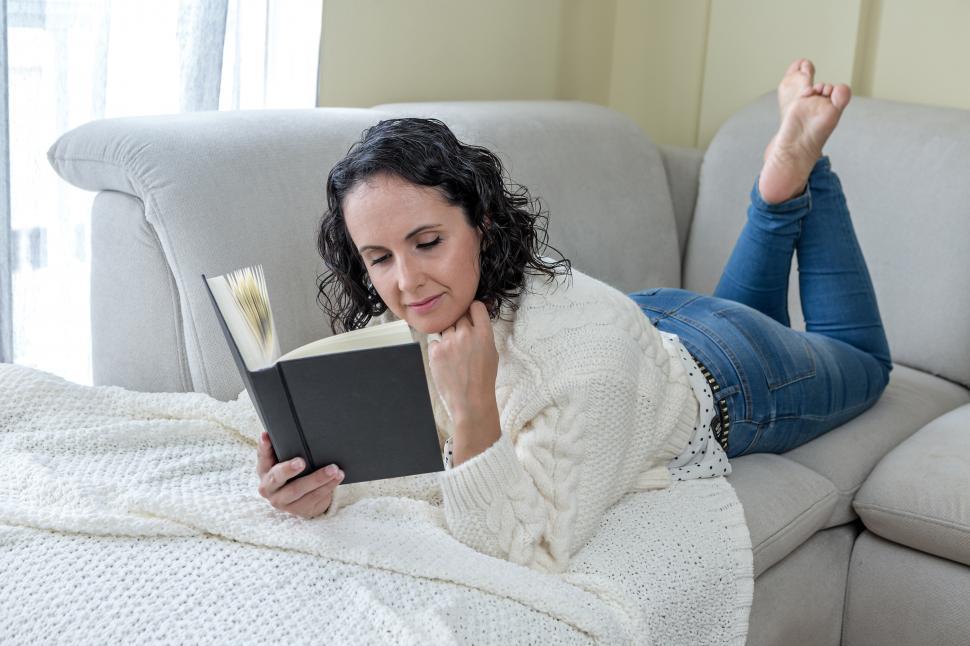Free Image of Young brunette woman lying on the sofa at home reading a book 