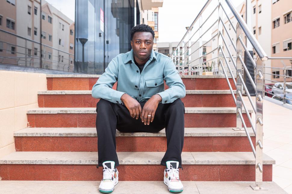 Free Image of Trendy black man resting on street stairs and looking at camera 