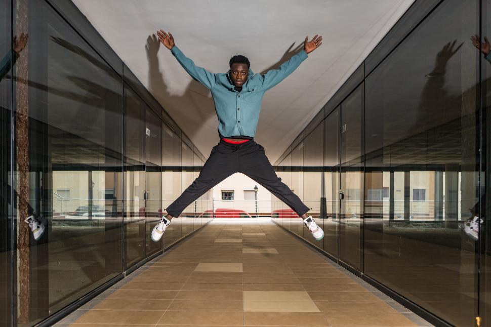 Download Free Stock Photo of Trendy serious black man jumping in passage and looking at camer 