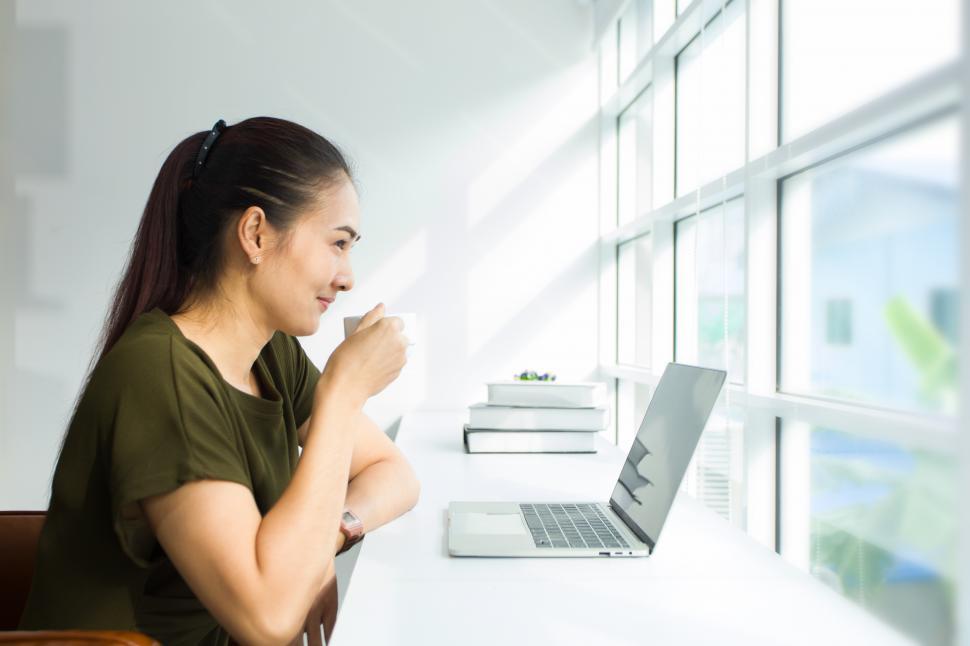 Free Image of Young woman sipping coffee, with laptop, near window 