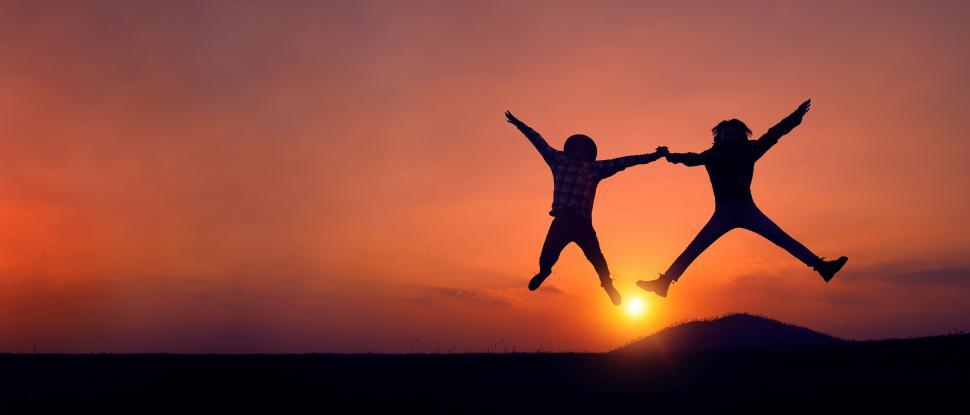 Free Image of Silhouette of two people jumping joyfully at sunset. 