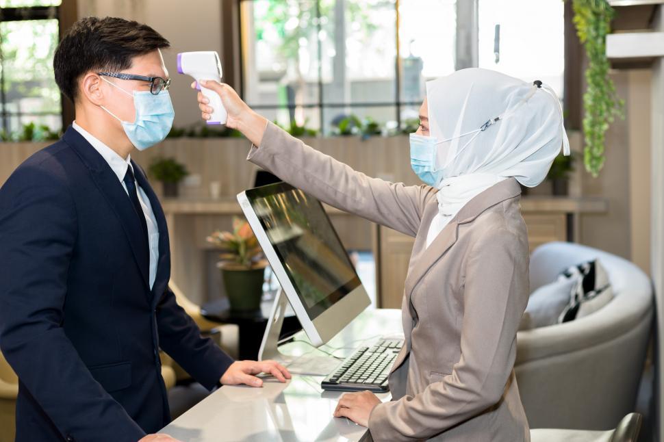 Free Image of Muslim female receptionist measures tourists temperature 