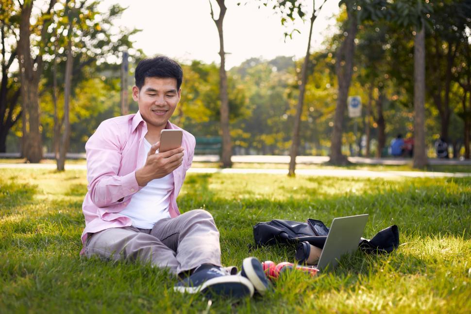 Free Image of Asian freelance man sitting in a park using his phone 