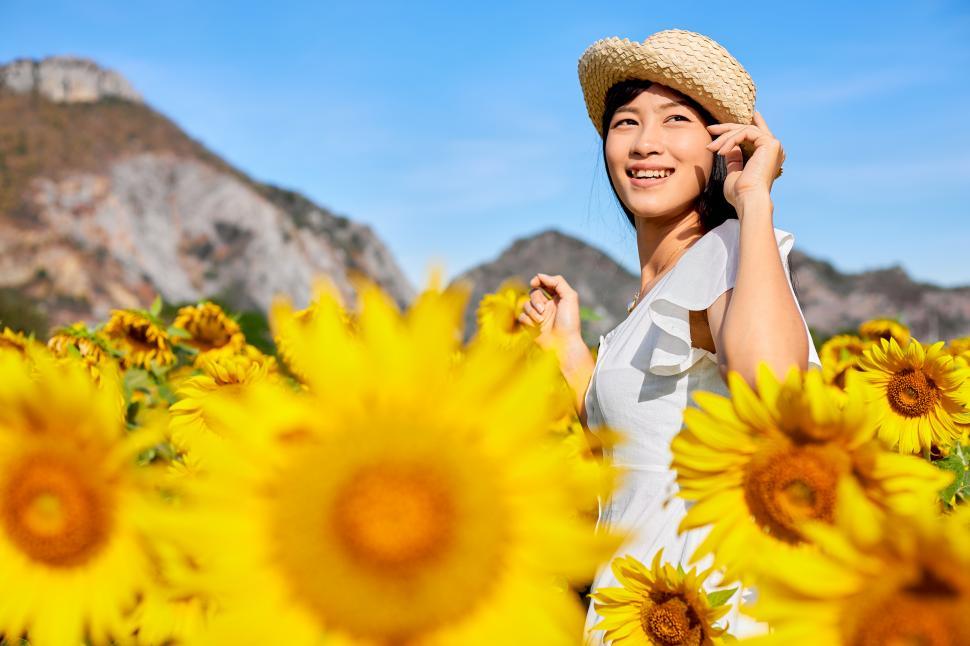 Free Image of A young woman in a straw hat stands in a sunflower field 