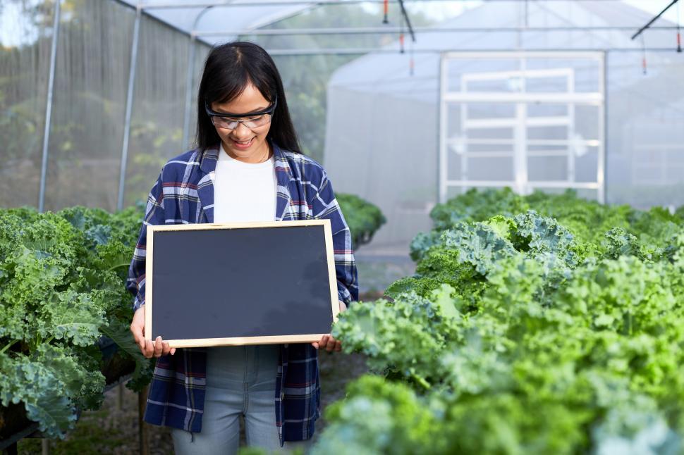 Free Image of Young female farmer with blank board sign in the greenhouse 