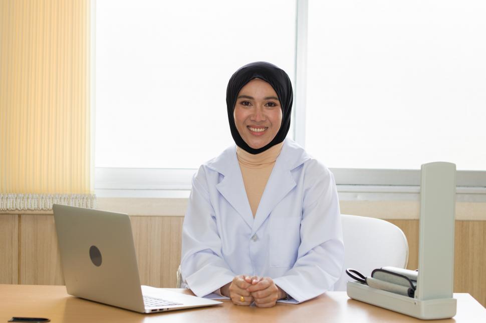 Download Free Stock Photo of Female doctor wearing a hijab sits at a table waiting for patient 