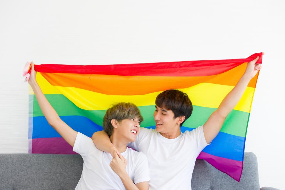 Free Image of Happy Asian couple holding up a rainbow flag. 