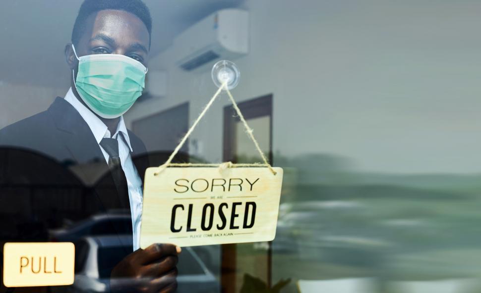 Download Free Stock Photo of Male waiter wearing an anti-virus mask flips sign to Closed 