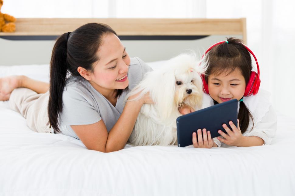 Free Image of Asian mother and daughter using tablet on bed with dog. 