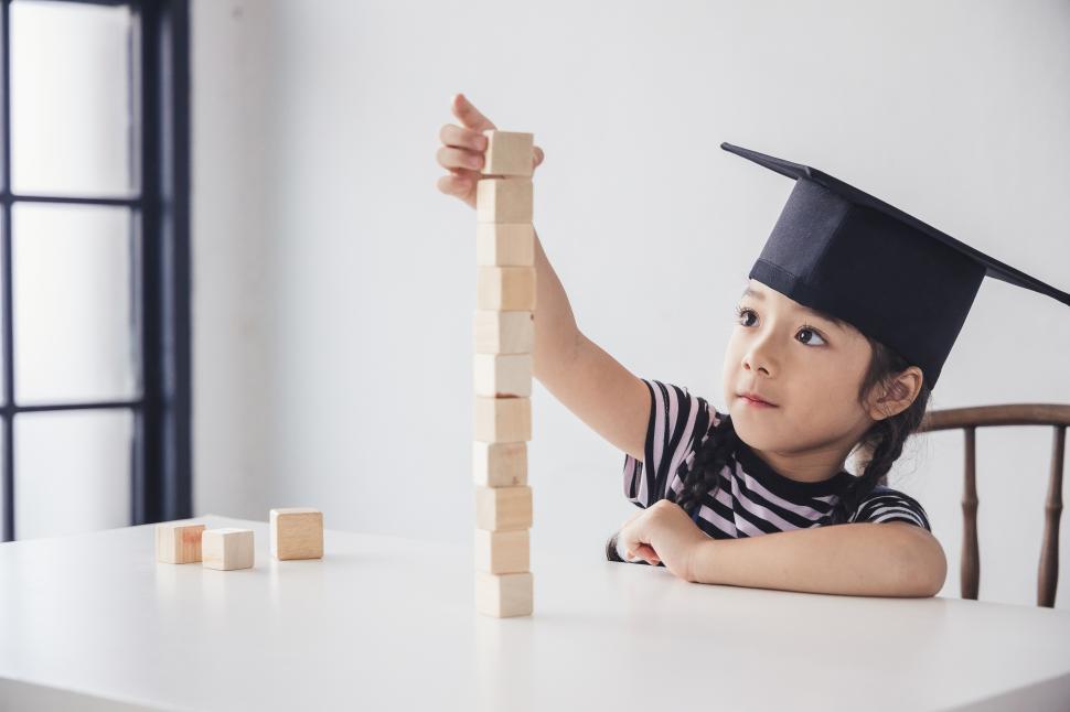 Free Image of Little girl in a mortarboard cap stacks blocks 