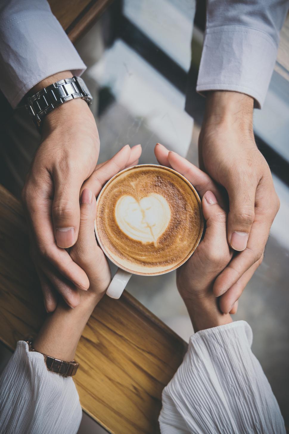 Free Image of Top view of a young lovers hand holding coffee with heart design 