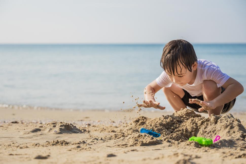 Download Free Stock Photo of Little boy digs in sand at sea shore 