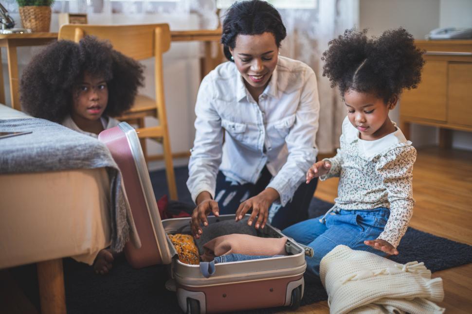 Free Image of Mom and daughters pack clothes into a suitcase 