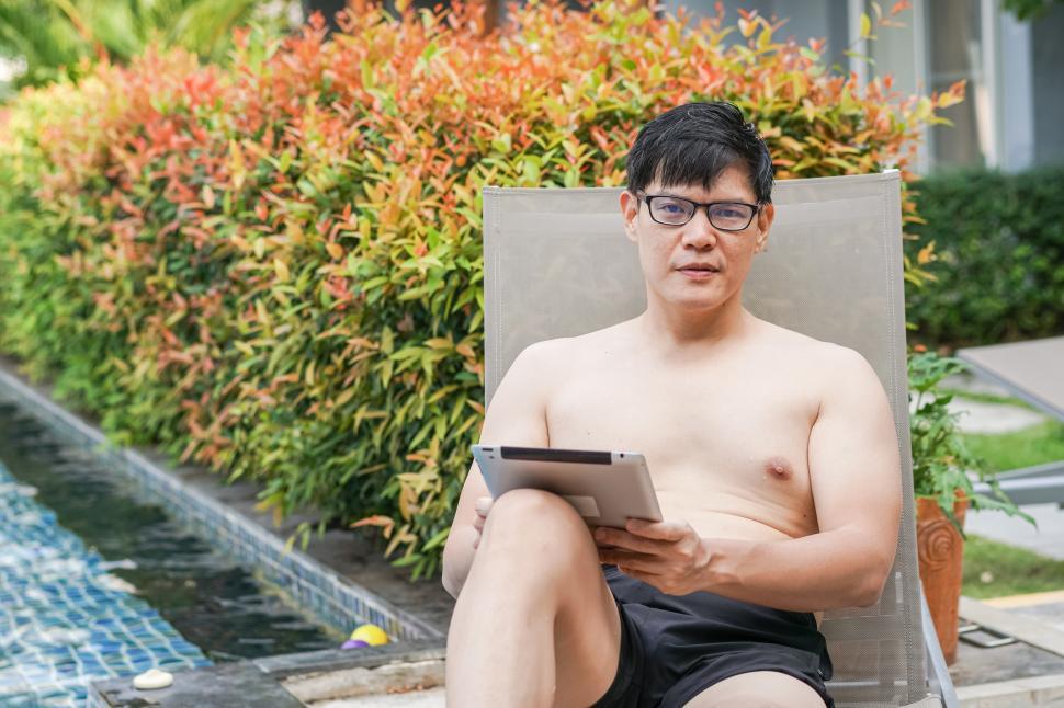 Free Image of Man in swimwear sitting by swimming pool 