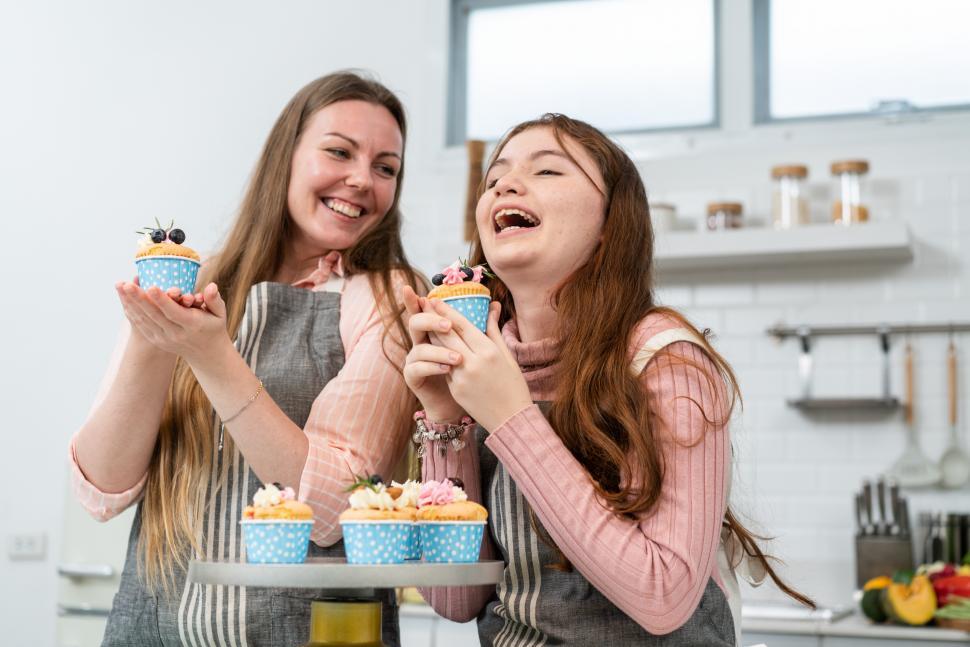 Free Image of Little girl laughing and holding homemade cupcake with mother 