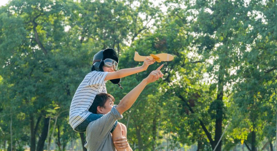 Free Image of Boy wearing pilot helmet playing with airplane, sitting on fathers shoulders 