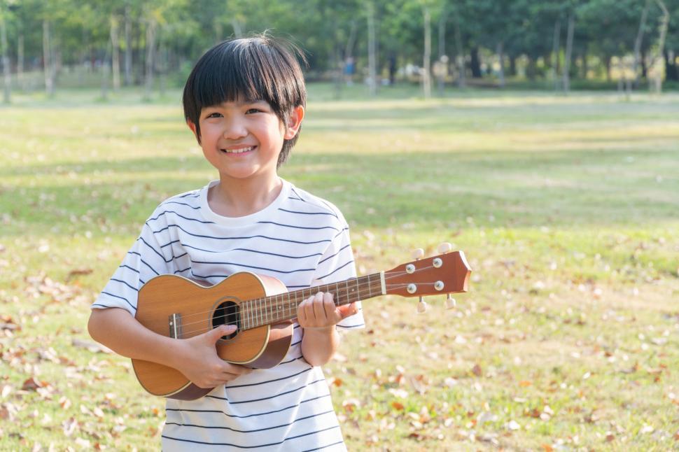 Free Image of Happy Asian boy playing on ukulele in the park 