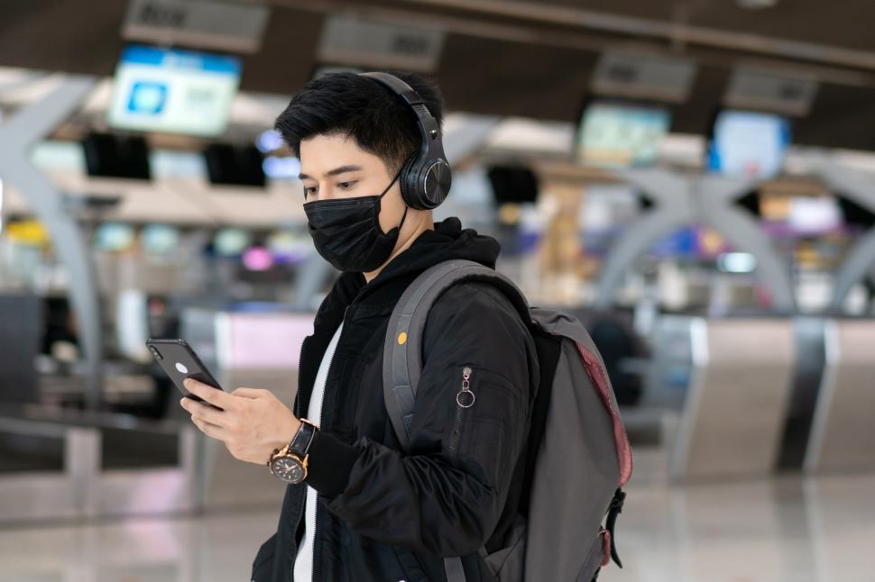 Free Image of Young man wearing mask with headphone listen to music at the airport 
