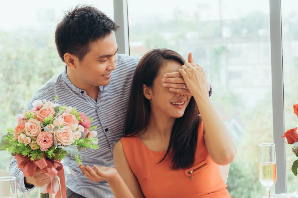 Free Image of Man closing girlfriend eyes to surprise with roses at a restaurant 