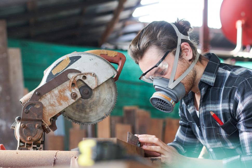 Download Free Stock Photo of Male carpenter wearing protective mask using electric circular chop saw 
