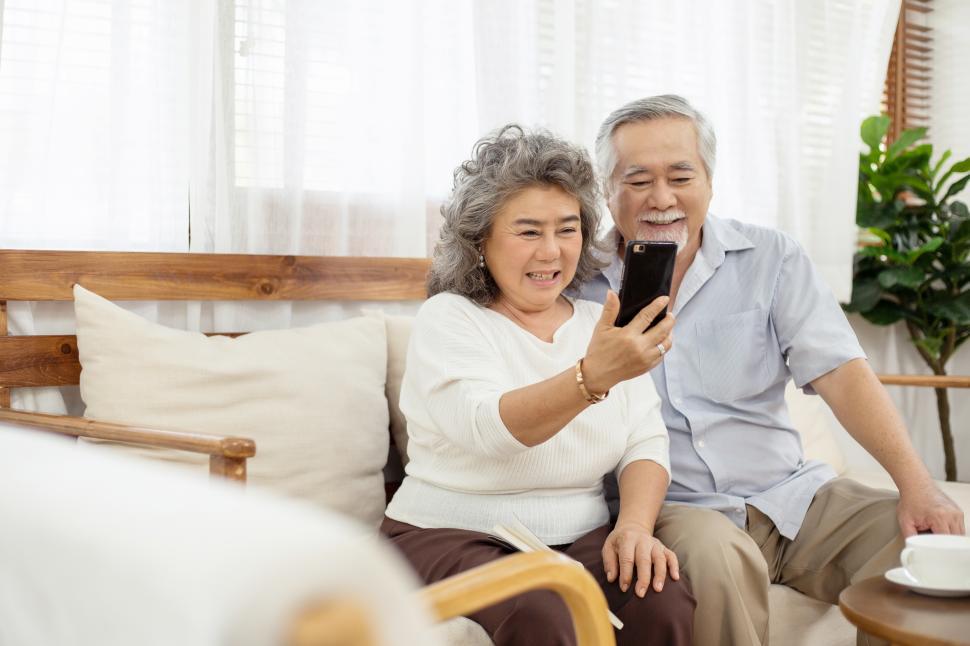 Free Image of Happy couple sitting on sofa using smartphone video call 
