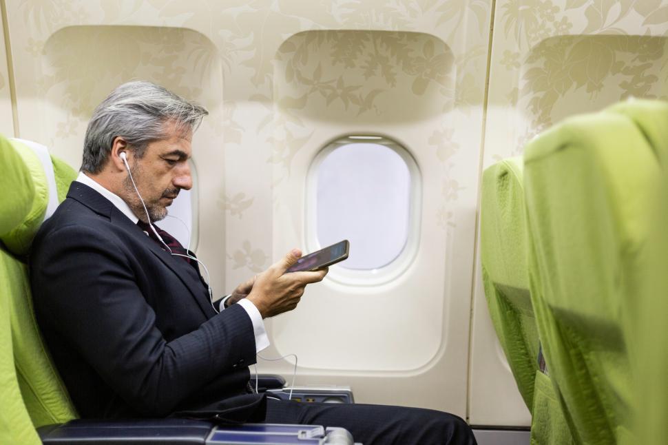 Free Image of Businessman watching movie on mobile on airplane 