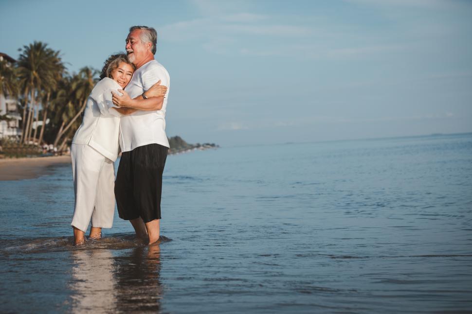 Free Image of Senior couple hugging while standing on in shallow surf 